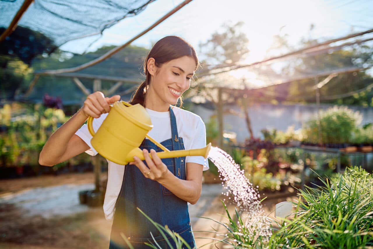 Smiling, allergy symptom-free gardener watering plants in a humid greenhouse.
