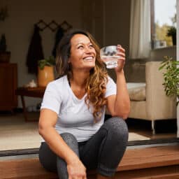 Happy, confident woman sitting on her patio at home drinking water.