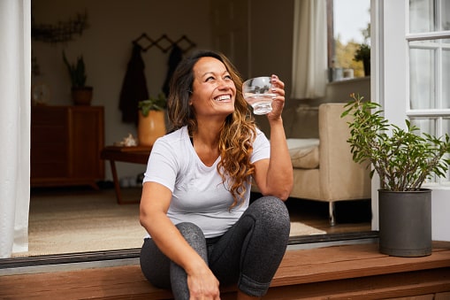 Happy, confident woman sitting on her patio at home drinking water.