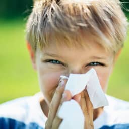 Portrait of a young child with seasonal allergies, blowing their nose in a field.