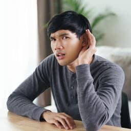 Man cups a hand around his ear with a confused expression; he is having difficulty hearing.