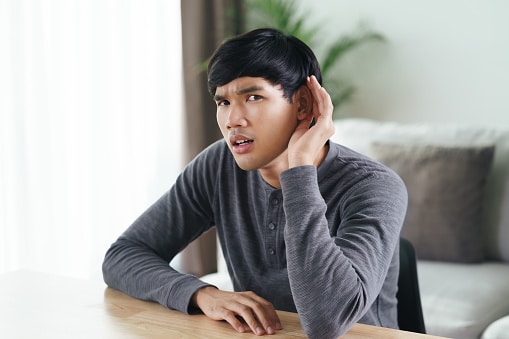 Man cups a hand around his ear with a confused expression; he is having difficulty hearing.