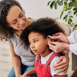 Cute girl with her mother during install hearing aid by her audiologist. Hearing treatment for a child